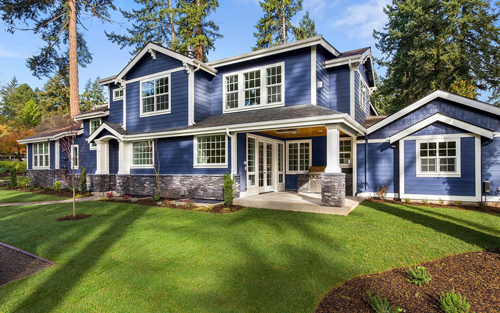 Facade of home that has been updated with siding contractors with manicured lawn, and backdrop of trees and blue sky